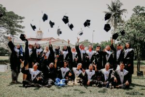 A joyful group of graduates celebrating outdoors, tossing caps in the air.